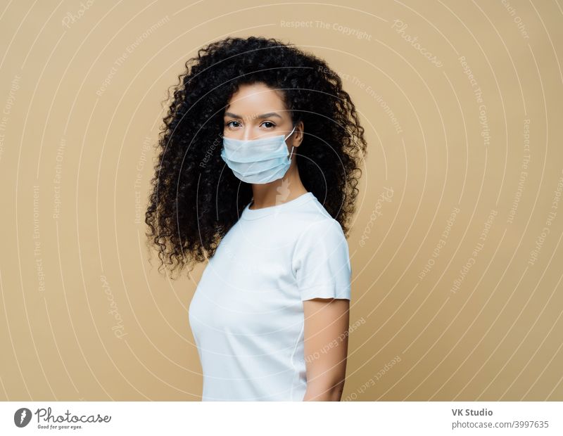 Seitliche Aufnahme einer Afroamerikanerin trägt schützende Gesichtsmaske, schützt vor Verbreitung der Coronavirus-Krankheit, bleibt zu Hause, befolgt Regeln der Selbstisolierung. Covid-19, Sicherheit, Quarantäne-Konzept
