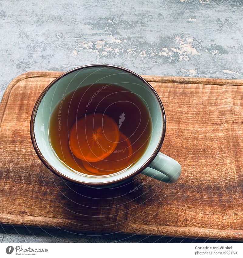 Eine Tasse mit heißem Darjeeling Tee und Zitronenscheiben steht auf einem Holzbrett. Grauer marmorierter Untergrund, Aufnahme aus der Vogelperspektive Teetasse