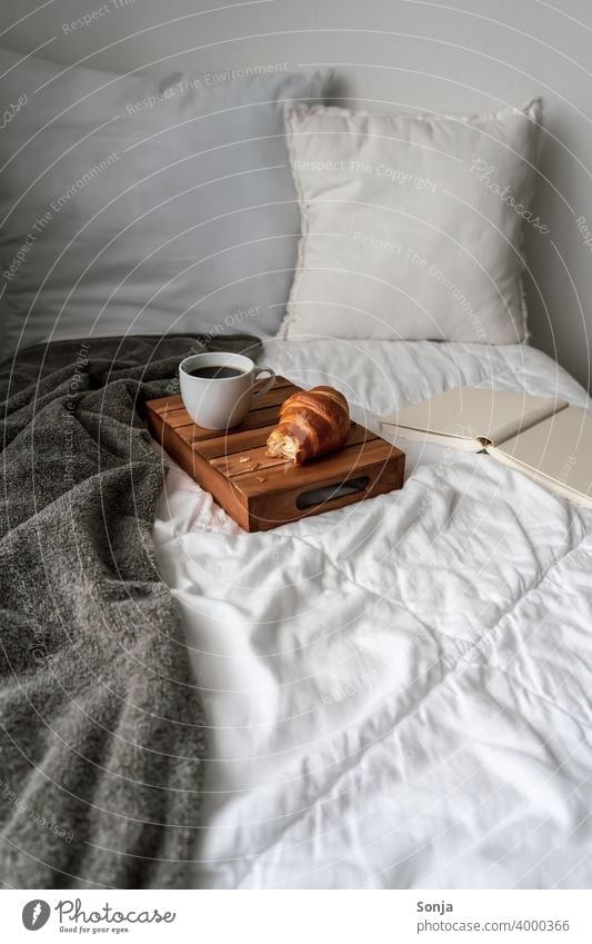 Frühstück im Bett mit einer Tasse Kaffee und einem Croissant Hygge Lifestyle Morgen zuhause Bettwäsche Kissen Buch Serviertablett Holz Wochenende Erholung heiß
