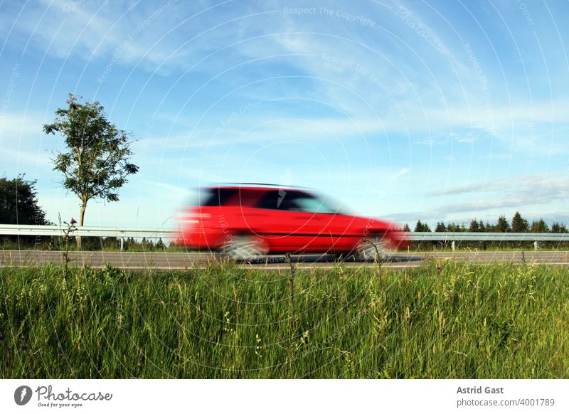 Schnelles Fahren auf deutschen Straßen. Ein rotes Auto rast eine Straße entlang auto fahren autofahren straße rasen raser schnell schnelles rasant deutschland