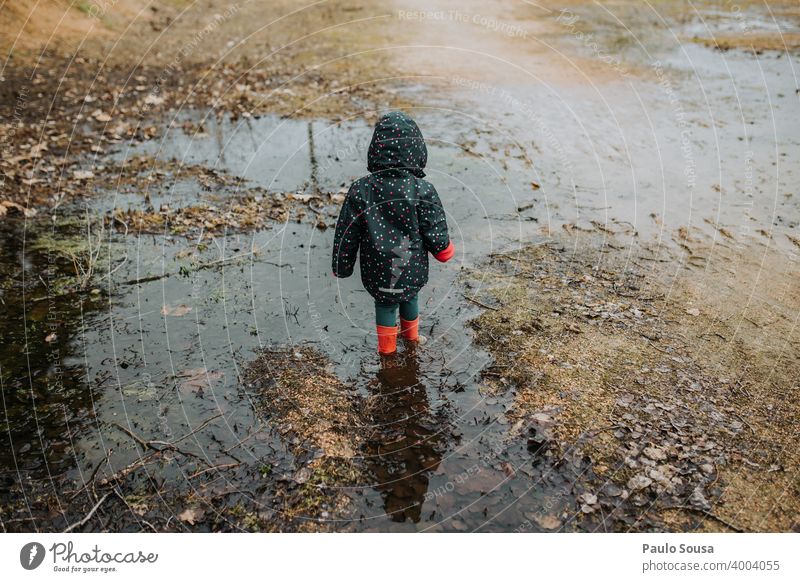 Kind mit roten Gummistiefeln spielt auf einer Pfütze Kindheit Mädchen Wasser Mensch Stiefel Spielen Regen dreckig Tag Textfreiraum unten Kleinkind