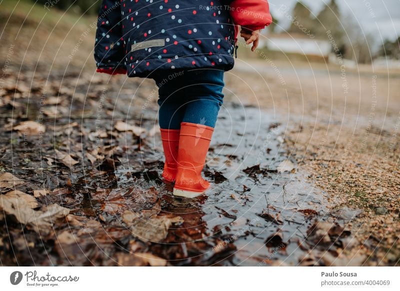 Niedriger Ausschnitt Kind mit roten Gummistiefeln geht auf Pfütze Kindheit authentisch Spielen Außenaufnahme Herbst dreckig Tag Wasser nass Mensch Freude