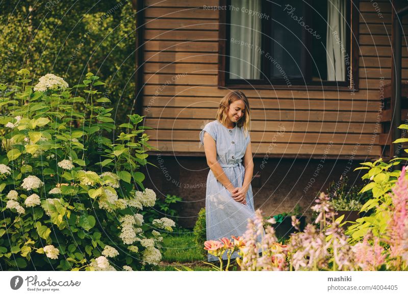 Junge glückliche Frau, die in einem privaten Garten spazieren geht, posiert an einem hölzernen Landhaus. Gartenarbeit Pflanze Glück Kaukasier Lifestyle Gärtner