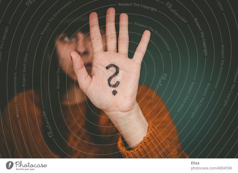 Eine Frau hält ihre Hand, auf die ein Fragezeichen gemalt ist, hoch. ratlos Verwirrung Identität Unsicherheit Irritation Fragen unsicher Unentschlossenheit