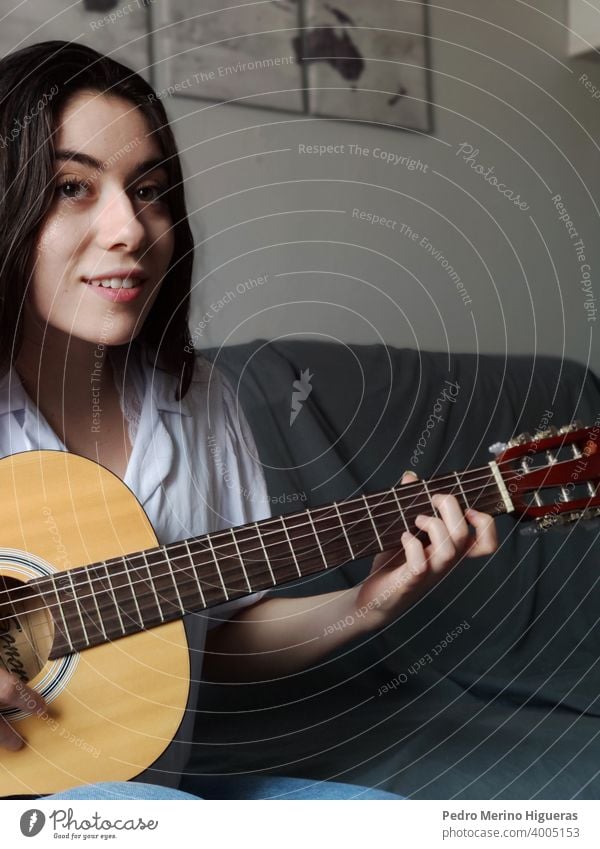 Frau spielt die Gitarre auf einem grauen Sofa Kaukasier Musical Musiker Mädchen Instrument Hintergrund Freizeitkleidung Schnur Atelier jung Lernen akustisch