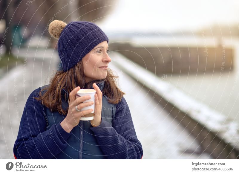 Glückliche brünette Frau mittleren Alters geht spazieren und trinkt einen Kaffee zum Mitnehmen trinken Getränk im Freien gehen Tee reif Lifestyle Generation