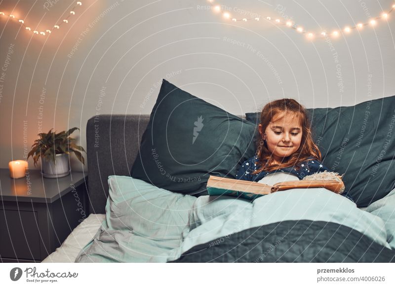 Kleines Mädchen lesen Buch und beobachten Bilder im Bett vor dem Schlafengehen. Gutenachtgeschichten für Kind Nacht Schlafenszeit Familie heimwärts Literatur