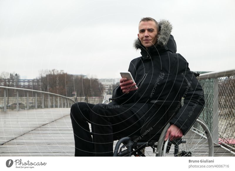 Konzept der behinderten Person. Mann in einem Rollstuhl draußen auf der Straße. Menschen mit Technologie mit Smartphone. Gerät querschnittsgelähmt verbunden