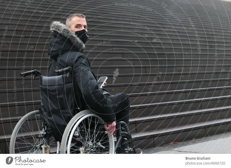 Konzept der behinderten Person. Mann in einem Rollstuhl draußen auf der Straße vor der Treppe. Menschen mit Smartphone. Operationsmaske deaktiviert