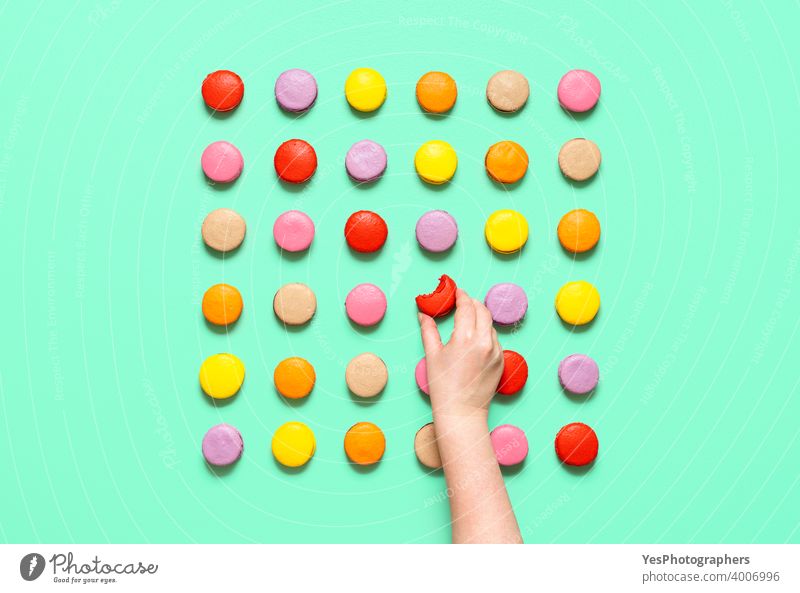 Macarons symmetrisch auf einem farbigen Hintergrund ausgerichtet. Frau Hand nimmt eine Makrone, Ansicht von oben obere Ansicht Mandelplätzchen Handwerklich