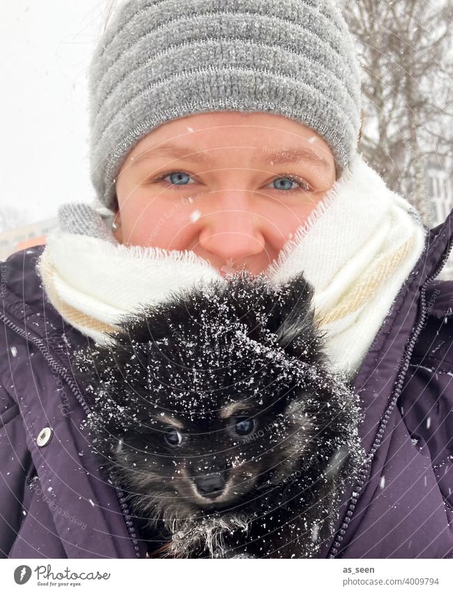 Junge Frau trägt Black Pomeranian Welpen durch den Schnee Zwergspitz Hunderasse blaue augen Blick in die Kamera Freude Tierliebe Schneeflocke Farbfoto