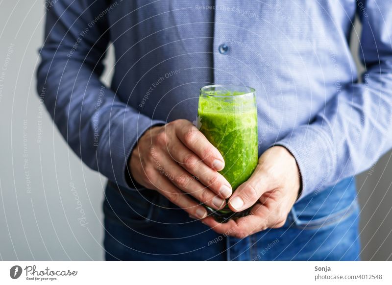 Mann hält ein Glas grünen Smoothie in seinen Händen smoothie 50 plus Hemd Jeanshose Teilansicht Hand halten Business Gesunde Ernährung Vitamin Diät