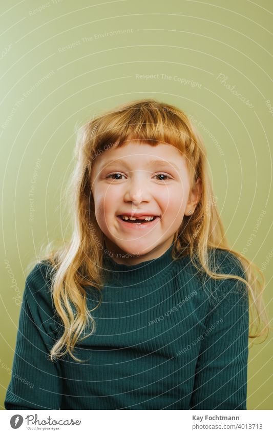 Porträt eines lachenden blonden Mädchens vor grünem Hintergrund Pony blondes Haar Freizeitkleidung Kind Kindheit farbiger Hintergrund niedlich Tochter Emotion