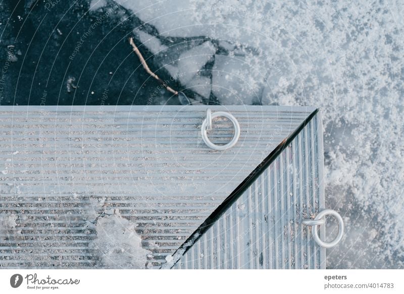 Kante eines Stegs über gefrorenem Wasser an einem See grau ultimatives Grau blau Eis Schnee Winter kalt Ring Ringe Scheidung Kälte weiß hell Eisscholle