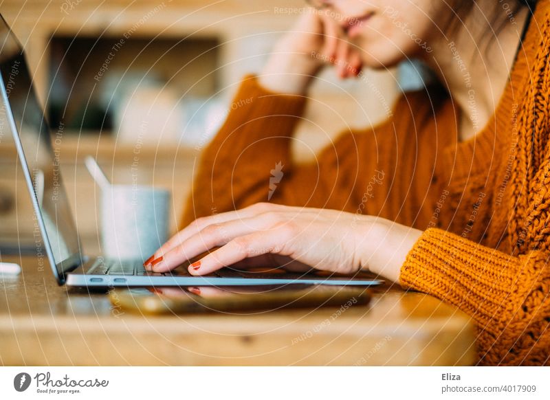 Junge Frau sitzt zuhause am Tisch und tippt etwas auf dem Notebook Laptop online surfen arbeiten Homeoffice home office tippen Computer modern Lifestyle