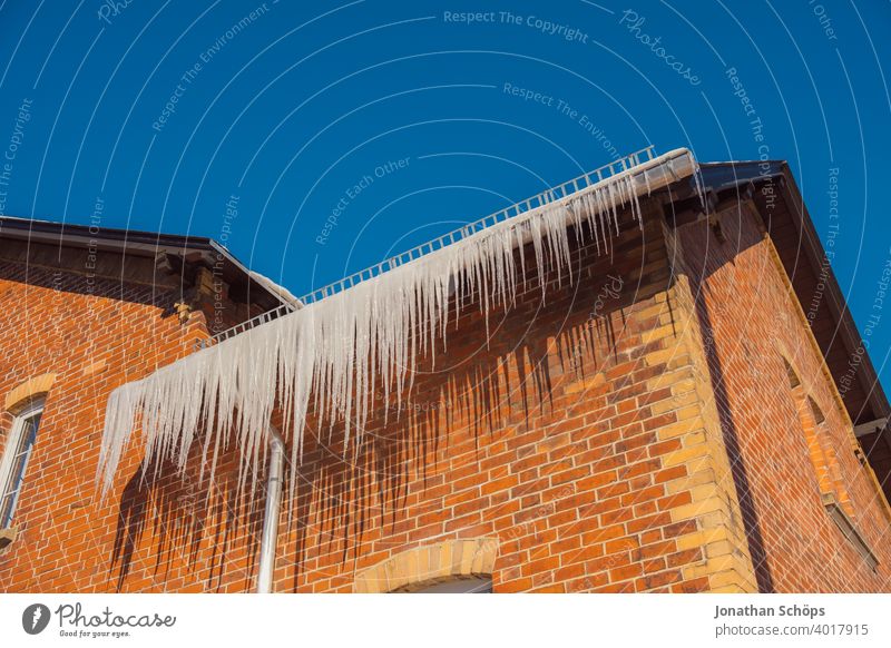 lange Eiszapfen an Dachrinne eines Backsteinhauses im Winter bei eisiger Kälte und Sonne architektur backstein Backsteinhaussiedlung Dachkante dachrinne