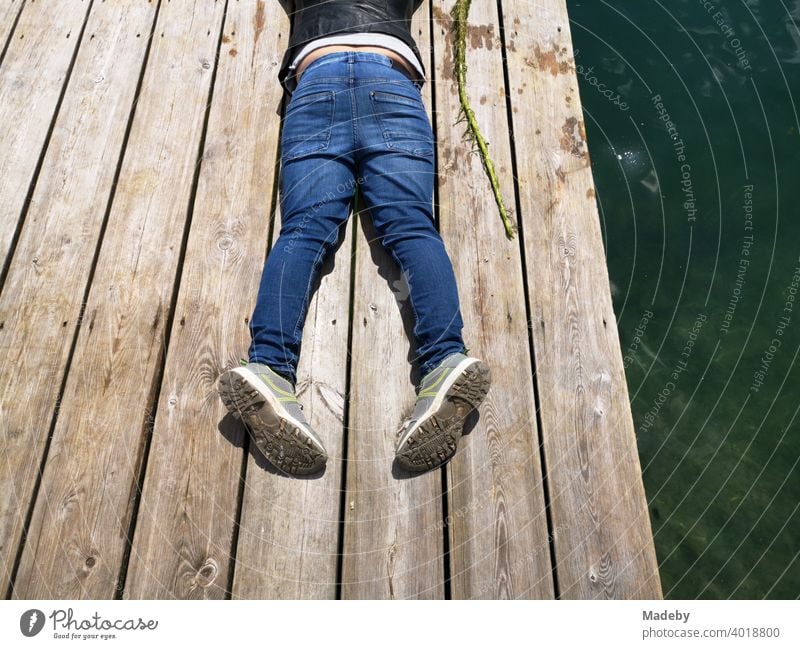 Junge in blauen Jeans auf einem Bootssteg aus rustikalem Holz am Lippesee im Sommer in Paderborn in Ostwestfalen-Lippe Holzsteg Badesteg Blue Jeans Steg