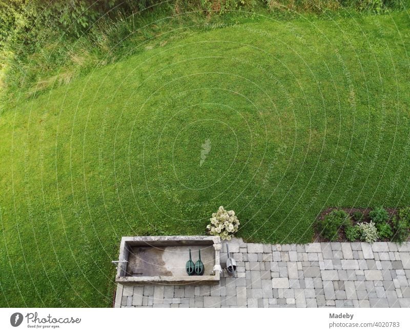 Grau gepflasterte Terrasse mit alter Viehtränke und grünem Rasen vor einem Bauernhaus in Rudersau bei Rottenbuch im Kreis Weilheim-Schongau in Oberbayern Wiese