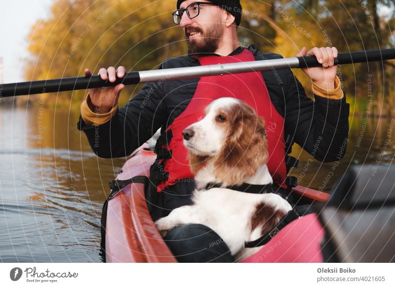 Glücklicher Mann rudert ein Kanu mit seinem Spaniel Hund, sonniges Herbstwetter. Going Kajak Bootfahren mit Hunden auf dem Fluss, aktive Haustiere, gesunde Hund und Besitzer auf ein Abenteuer