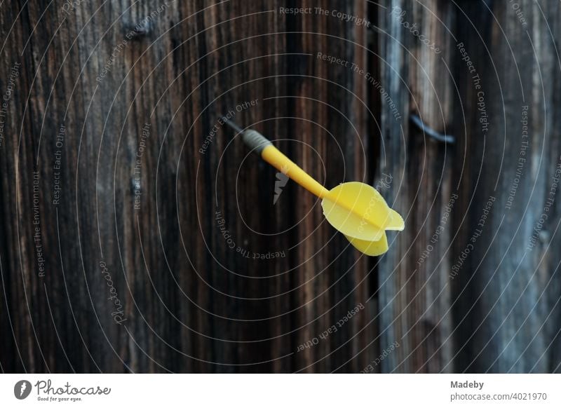 Gelber Dartpfeil im braunen Holz einer alten Scheune auf einem Bauernhof in Rudersau bei Rottenbuch im Kreis Weilheim-Schongau in Oberbayern Pfeil Spiel