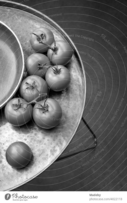Frische Tomaten neben einer Schale auf einem dekorativen runden Tablett mit Füßen in einer Designerwohnung in Rudersau bei Rottenbuch im Kreis Weilheim-Schongau in Oberbayern, fotografiert in klassischem Schwarzweiß