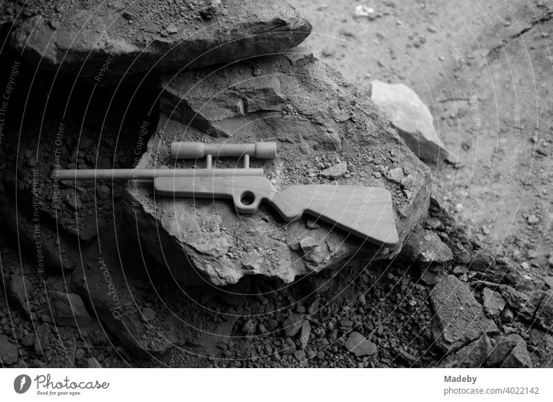 Spielzeuggewehr aus Holz mit Zielfernrohr auf zerbröselndem Gestein einem alten Bauernhaus in Rudersau bei Rottenbuch im Kreis Weilheim-Schongau in Oberbayern, fotografiert in klassischem Schwarzweiß