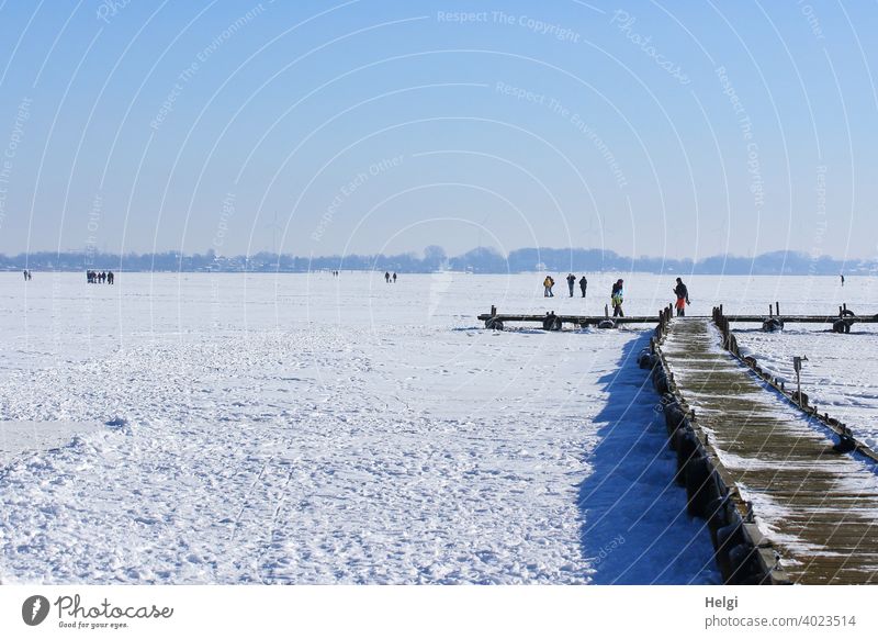 zugefrorener See mit Schnee, Holzsteg und Menschen, die auf dem Eis stehen und gehen Winter Kälte frieren Dümmer See Steg Weite Licht Schatten Sonnenlicht