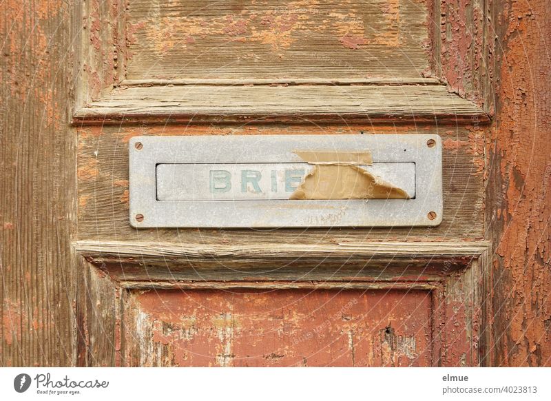 alter, beklebter Briefkastenschlitz mit einer Klappe, auf der "BRIEFE" steht, aus Metall in einer alten Holztür, an der die braune Farbe abblättert / Brief schreiben / E-Mail / Briefkastenfirma