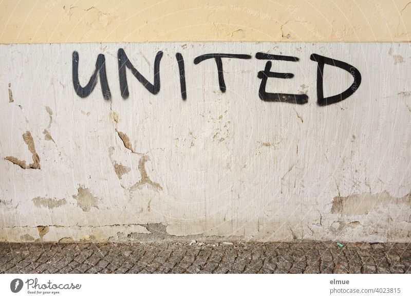 "UNITED" steht in schwarzen Großbuchstaben an der grauen, alten, verputzten Wand / verbunden / Schmiererei united vereint Fassade vereinigt Losung Graffito