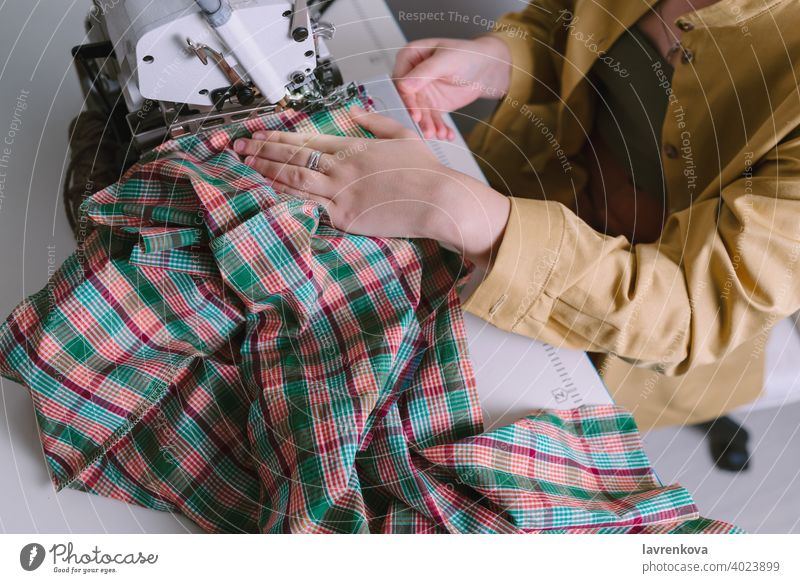 Draufsicht auf eine Frau bei der Arbeit an einer Overlock-Nähmaschine in ihrer Werkstatt, Bekleidung Material Gewebe Nähen kreativ Faser Sitzen Werkzeug