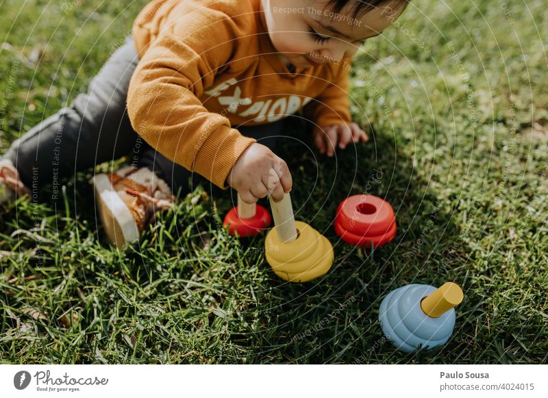 Kind spielt mit Spielzeug im Gras Holz hölzern 1-3 Jahre Kaukasier sitzen Sitzen Kleinkind Mensch Kindheit Farbfoto Spielen Tag Freude Außenaufnahme niedlich