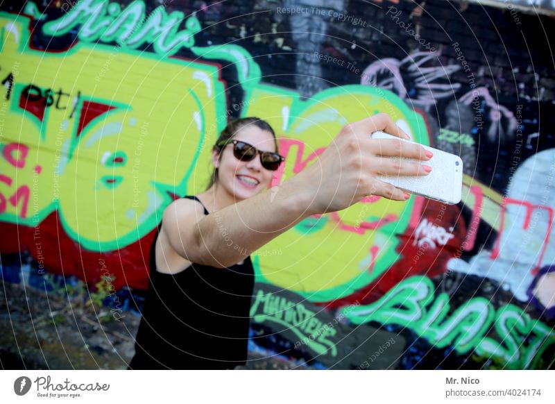 Junge Frau macht ein Selfie vor einer Graffiti Wand Smartphone Eitelkeit jung Selbstportrait Gesicht Telefon Handy Mobiltelefon kamera posen Pose posieren