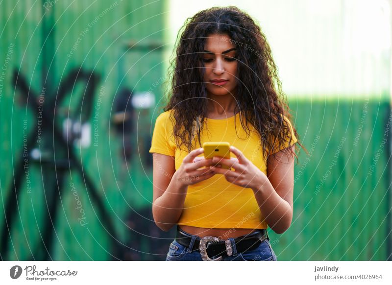 Junge arabische Frau geht auf der Straße mit ihrem Smartphone jung Texten Nachricht Tippen gelb copyspace Mädchen Aufnahme Frisur attraktiv schön urban