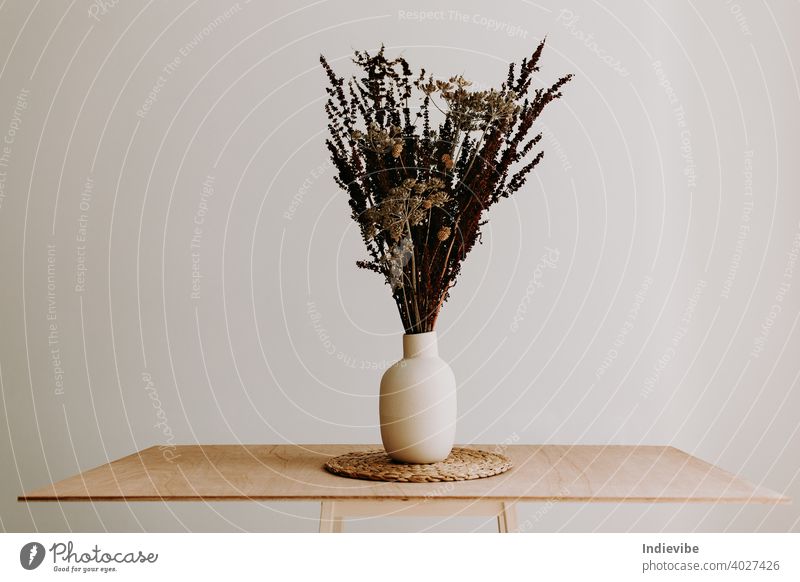 Ein Strauß wilder getrockneter Blumen in einer weißen Keramikvase in Großaufnahme auf einem braunen Holztisch. Blumenstrauß Vase vereinzelt Frühling Natur