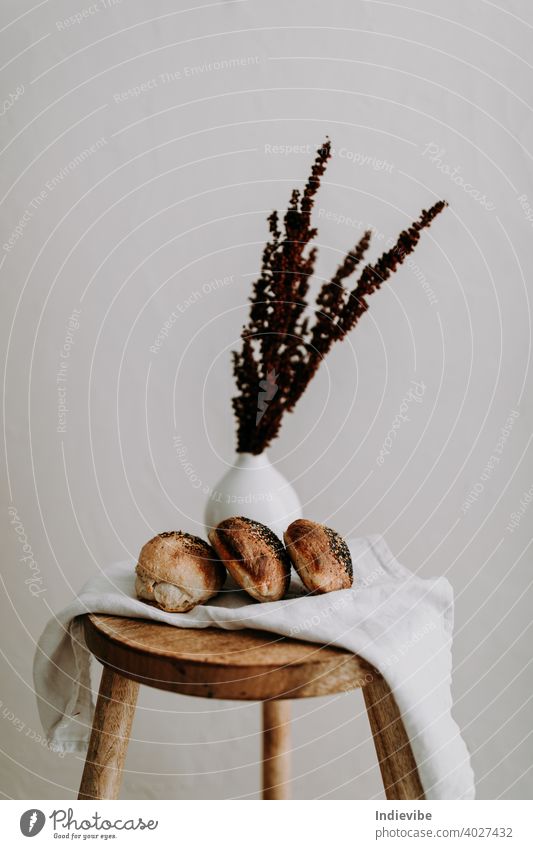 Drei Sauerteigbrötchen mit Mohn und Sesam auf einer Serviette auf einem Holzschemel, und getrocknete Wildblumen im Hintergrund Brötchen Frühstück Brot Gluten
