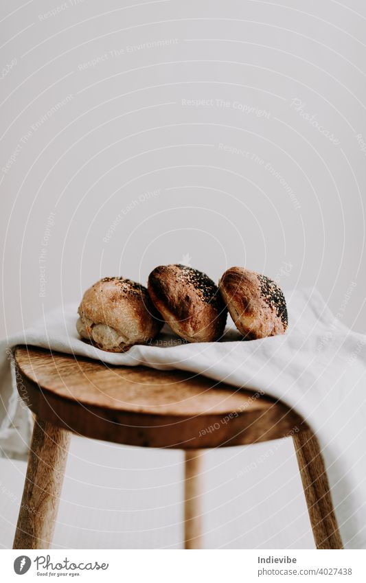 Drei Sauerteigbrötchen mit Mohn und Sesam auf einer Serviette auf einem Holzschemel Brötchen Frühstück Brot Gluten Gebäck Bäckerei frisch Morgen Mehl ganz