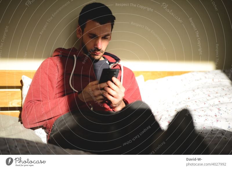 Mann mit Handy lesen benutzen Sonnenlicht Internet zu Hause zu Hause bleiben Quarantäne vertieft