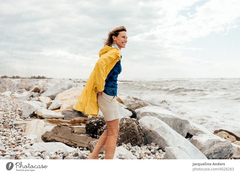 Frau mit wehenden Haaren in einem gelben Regenmantel schaut auf das Meer Meeresufer Wind gelber haare im wind glücklich Sommer Natur Freiheit