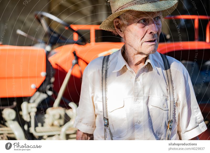 Porträt eines sehr alten Bauern mit Strohhut, der vor einem roten Traktor das Leben erklärt. Generation Erwachsener gealtert Ackerbau Auto Automobil PKW