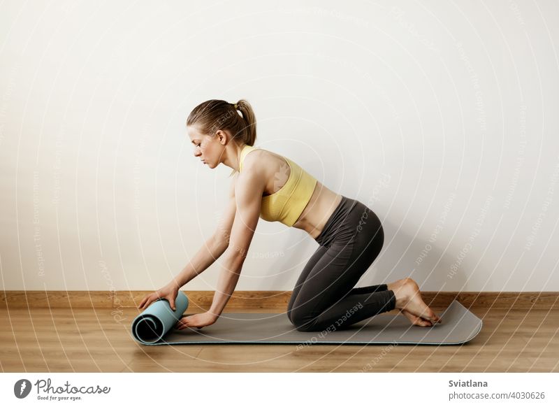 Ein junges Mädchen rollt eine Yogamatte aus, bevor sie eine Yogastunde nimmt. Yoga, Fitness, Lebensstil Pose Stehen Frau Körper Übung Atelier erweitert Seite
