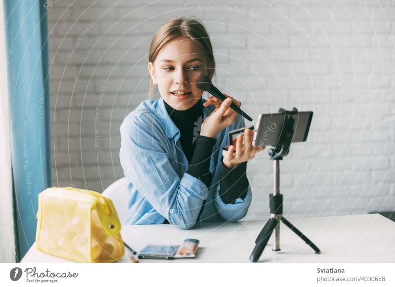 Ein Teenager-Mädchen schminkt sich und nimmt mit einem Smartphone auf einem Stativ zu Hause ein Video für ihren Blog auf. Kommunikation eines Video-Blogger-Mädchens in sozialen Netzwerken mit Abonnenten und Freunden