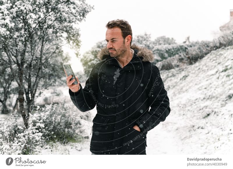 Mann durchsucht Smartphone im Winterwald Browsen Wald Schneefall benutzend warme Kleidung Wälder gutaussehend Oberbekleidung kalt Anschluss Mobile Internet