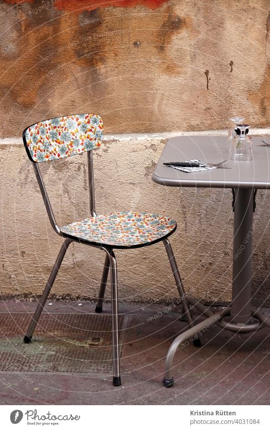 hübsch gemusterter stuhl im straßencafé tisch draußen wand fassade küchenstuhl retro vintage bistro restaurant gastronomie urban gläser besteck resopal