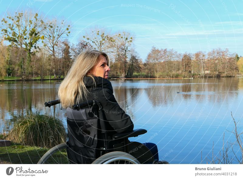 Konzept der behinderten Person. Eine Frau in einem Rollstuhl draußen in der Natur vor einem See. Erwachsener schön blondes Haar Kaukasier Kontemplation
