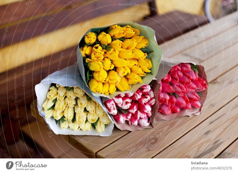 Mehrere Sträuße von Tulpen in verschiedenen Farben in Papierverpackung liegen auf einem Holztisch. Frauentag, Muttertag, Valentinstag. Ein Geschenk, Grußkarte, Platz für Text