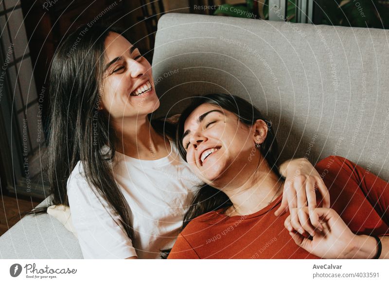 Ein lesbisches Paar lächelnd und lachend Spaß haben auf der Couch eines modernen Wohnung während umarmt einander mit Liebe anhänglich Antwort an Kuscheln