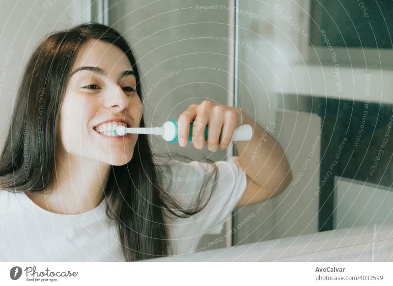 Eine junge Frau mit schwarzen Haaren putzt sich die Zähne mit einer elektrischen Zahnbürste Hygiene dental Bad bürstend Person Lächeln Glück im Innenbereich