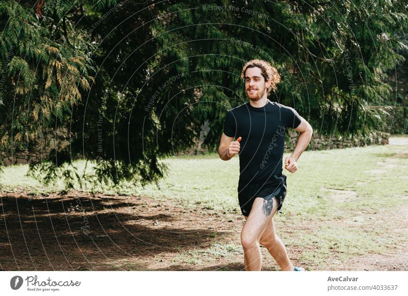 Ein langes Haar männlich läuft zwischen den Bäumen während eines sonnigen Tages im Park mit Kopie Raum 20s laufen trainiert. horizontal Marathon Läufer rennen