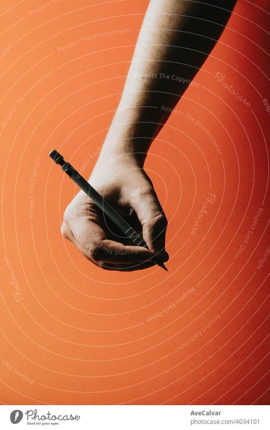 Eine junge Hand, die einen Druckbleistift über einen orangefarbenen Hintergrund mit tiefen Schatten ergreift Bleistift Büro Design Schreibstift Papier Bildung