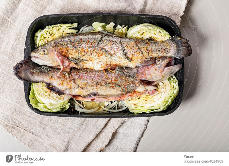 Frische Forelle mit Gewürzen und Gemüse. Süßwasserfisch mit Safran, roten Zwiebeln und Kraut in einer gusseisernen Auflaufform. Heller Hintergrund. Ansicht von oben. Platz zum Kopieren